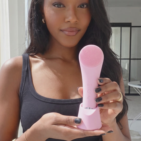 She Glow Heated Sonic Facial Cleansing Brush — blush pink silicone brush in charging stand